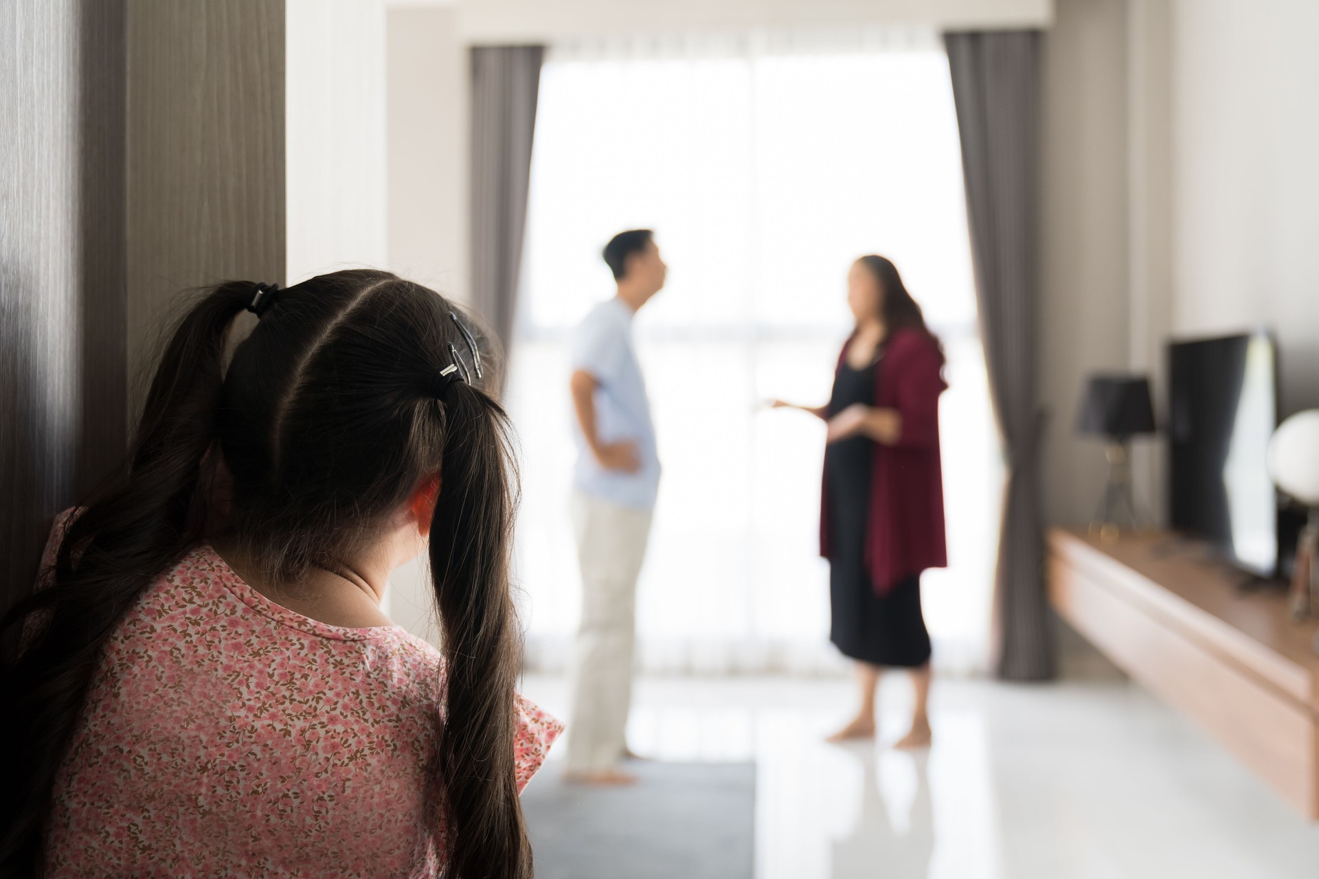 Back view of child girl crying at the door from father and mother arguing. Little girl crying because parents arguing blur background. family negative, quarrels concept. Back view of child girl crying at the door from father and mother arguing. Little girl crying because parents arguing blur background. family negative, quarrels concept.